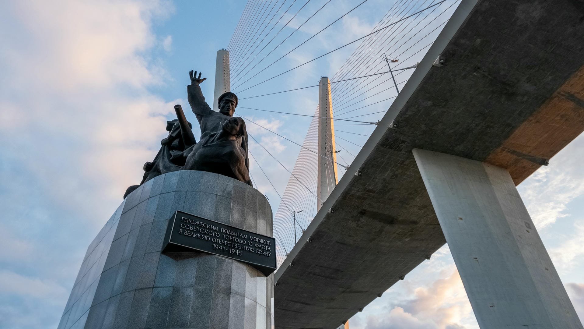 A modern sculpture located under a bridge, with a Russian plaque on its base.