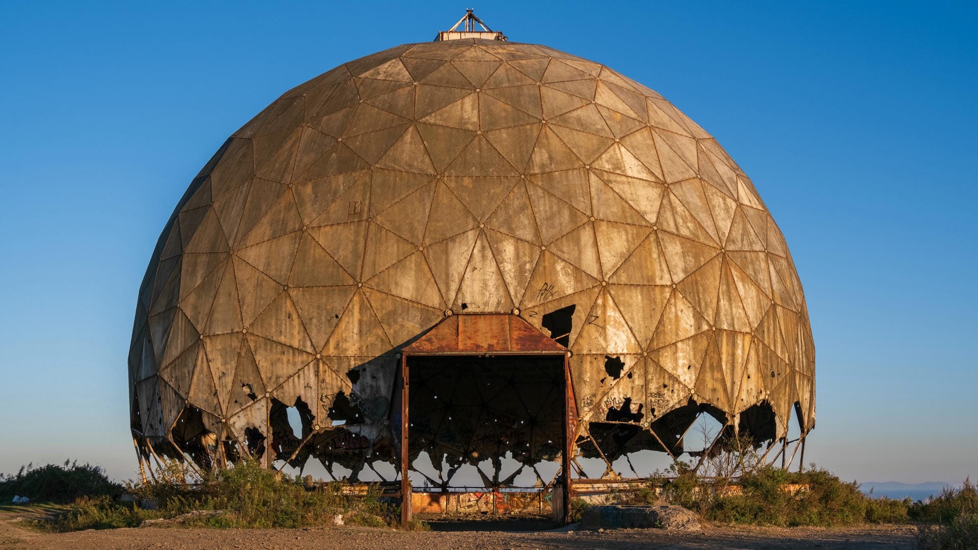 A dilapidated domed structure with a surface covered in rust and damage, featuring multiple openings at the base.