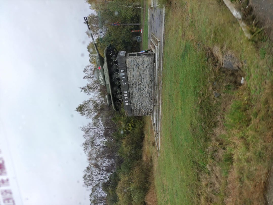 A tank monument featuring a red star symbol on the tank, surrounded by lawn and trees.