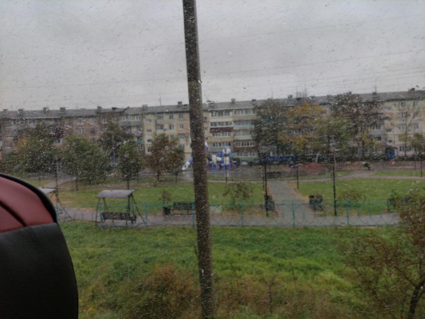 A residential area seen through a car window, with buildings in the distance and green spaces with playground facilities in the foreground.