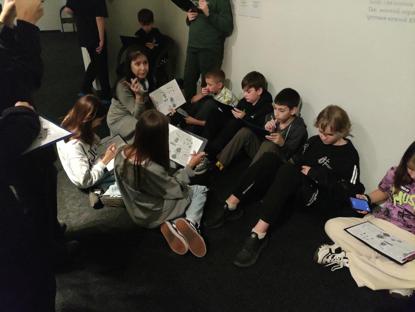 A group of children sitting on the ground, each holding a workbook.