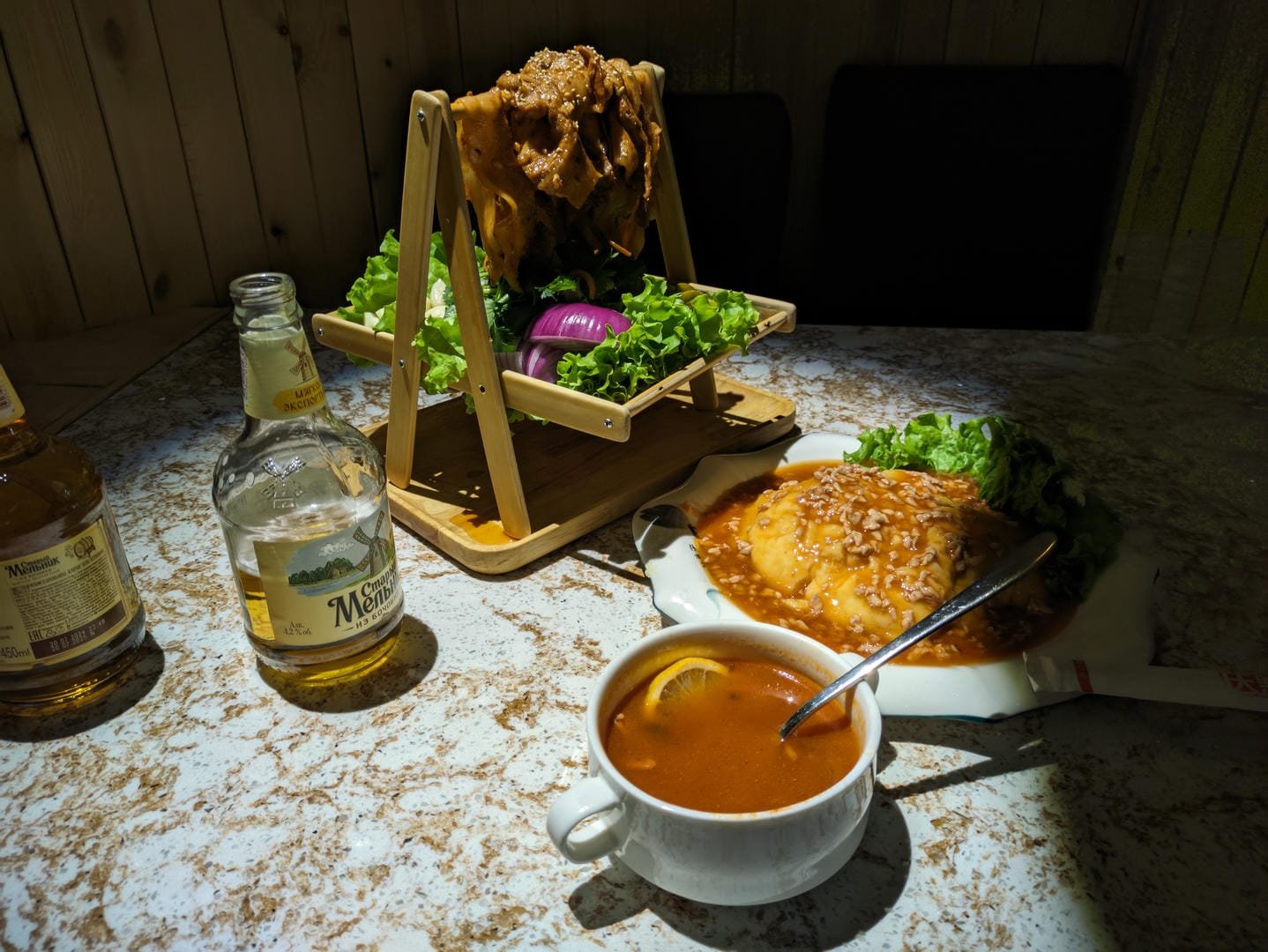 A bowl of soup, a meat dish, and a bottle of wine served on a dining table.