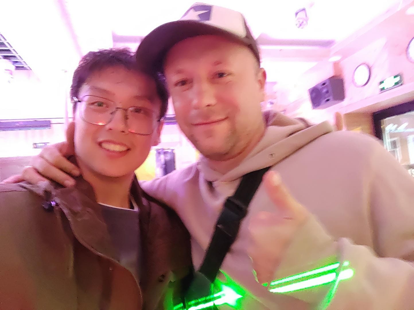 Two people taking an indoor selfie, with pink lighting and decorations in the background.