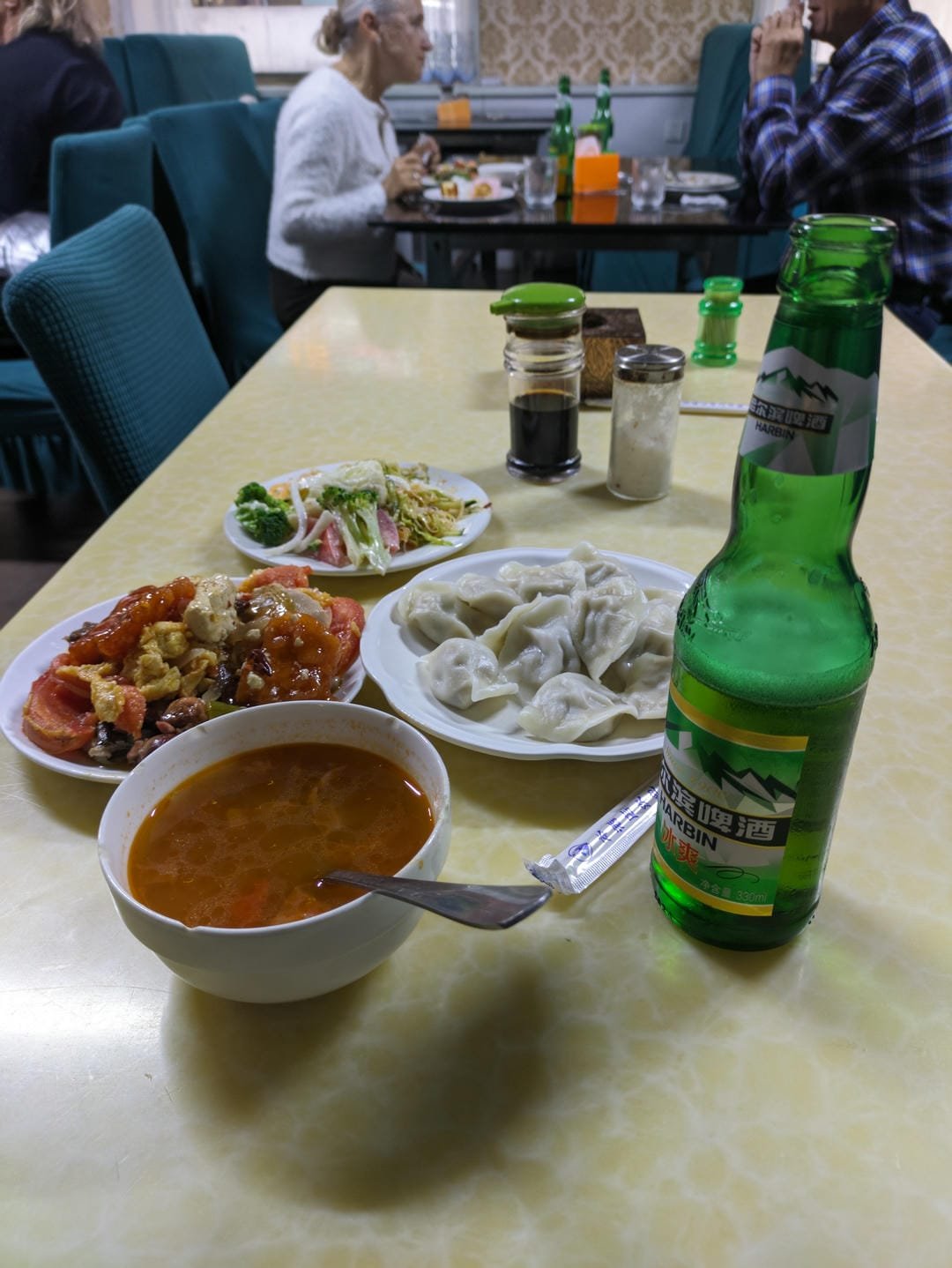 Dumplings, stir-fried dishes, soup, and a bottle of beer served on a dining table.