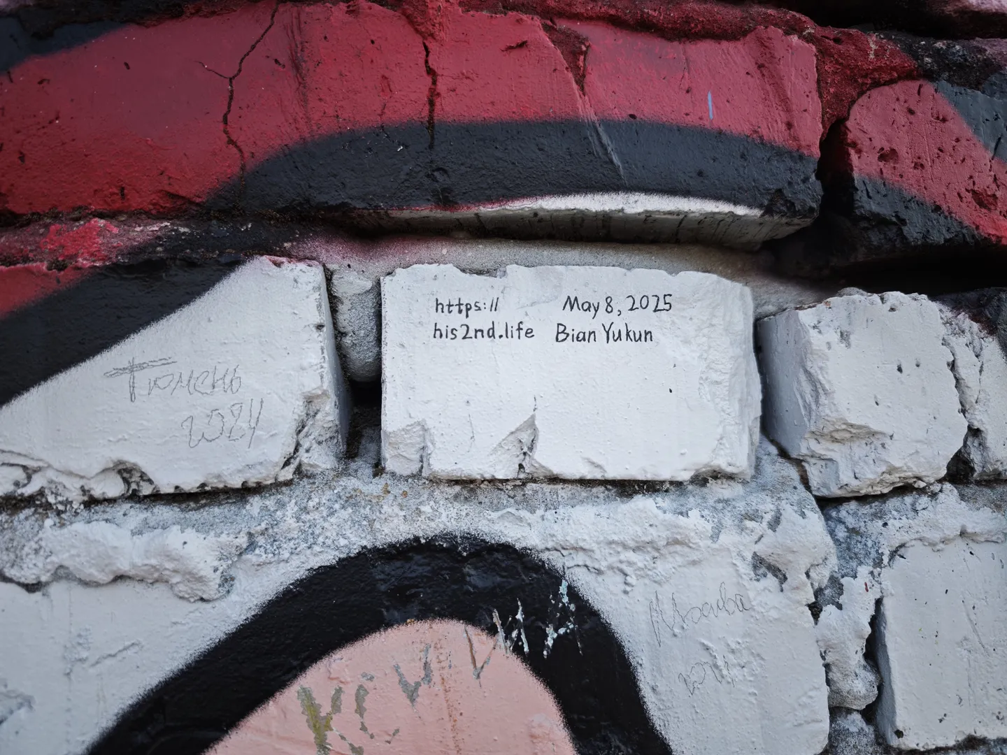 A white brick wall inscribed with the repeating text 'https://his2nd.life May 8, 2025 Bian Yukun', surrounded by red and black graffiti patterns.