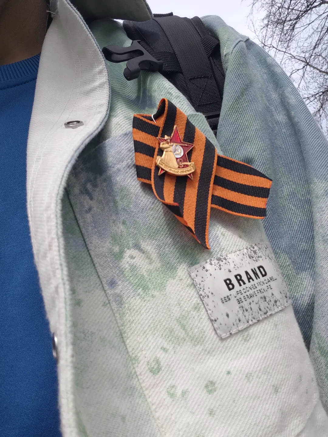 An orange-and-black striped St. George's ribbon and a red star medal pinned onto a light-colored jacket. The jacket has a blue lining and a brand label at the collar.