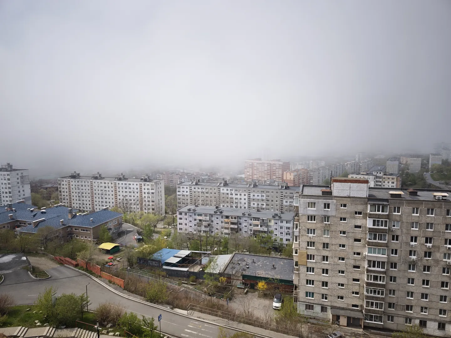 A residential area with neatly arranged multi-story buildings featuring colorful exterior walls. Roads and green belts run between the buildings, with vehicles driving on the roads under a sky filled with heavy fog, resulting in low visibility.